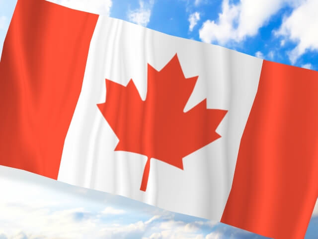 青い空と白い雲を背景に棚引くカナダ国旗