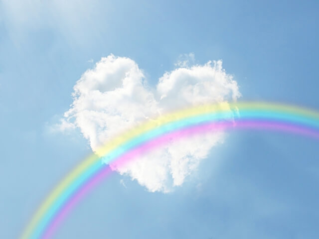 ハートの形をした白い雲の前に，弧を描く虹