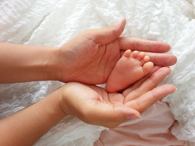 赤ちゃんの足を両手で掬い取るように支える母親の手