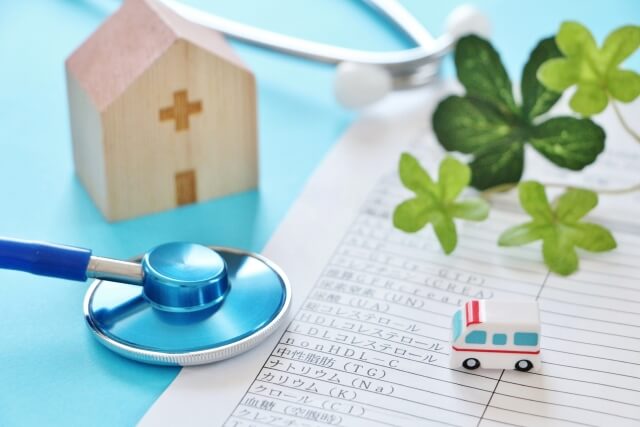 健康診断表の上に置かれた聴診器，木製の病院模型と救急車のおもちゃ，そして観葉植物