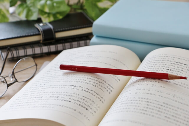 参考書（教材）の上に置かれた赤鉛筆と机上のメガネやシステム手帳