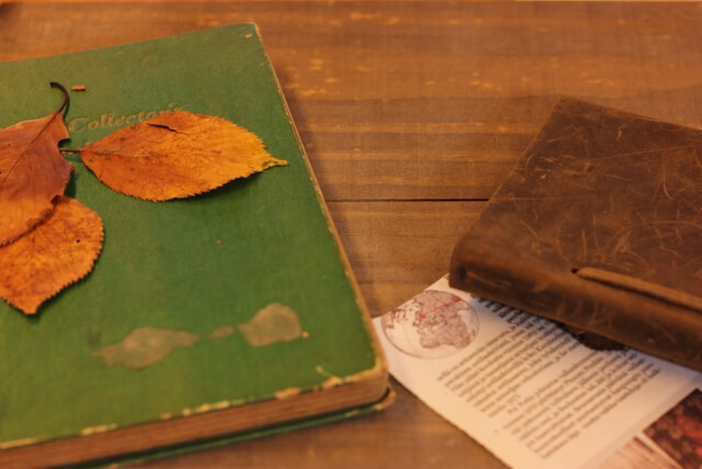 木目の机上に置かれた２冊の古い本。その１冊の表紙の上に置かれた３枚の紅葉した葉っぱ。