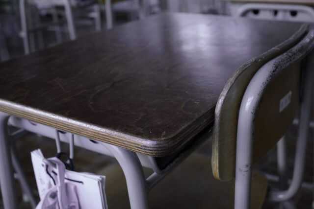 教室内で１つの机にきちんと収めされた１脚の椅子（モノトーン，いじめや不登校のイメージ）