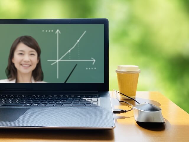 リモート授業で緑の前のテーブルに置いたノートパソコンに映る女子学生とグラフ